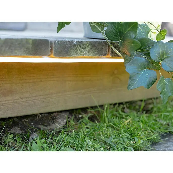 Garden 24 LED-Stripes - 3 m, Warmweiß - Die Holzterrasse ist mit einer LED-Leiste ausgestattet, die ein warmes, einladendes Licht spendet. Ein grüner Efeu rankt die Seite herauf.