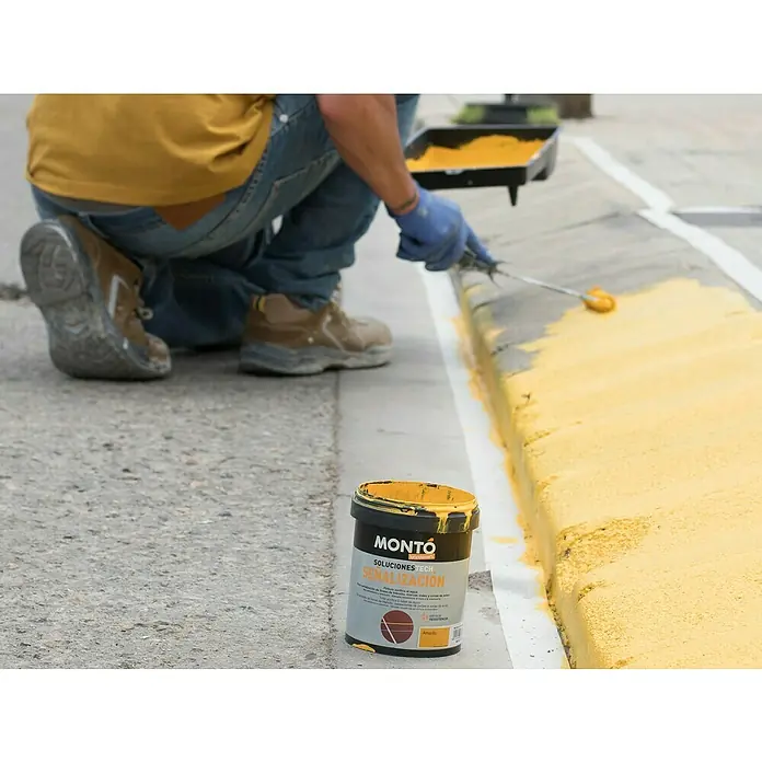 Montó Bricolovers Pintura de señalización Soluciones Tech - Amarillo, 750 ml - Un trabajador aplica pintura amarilla MONTO a un bordillo para mejorar la visibilidad. El bote de pintura MONTO está a su lado.