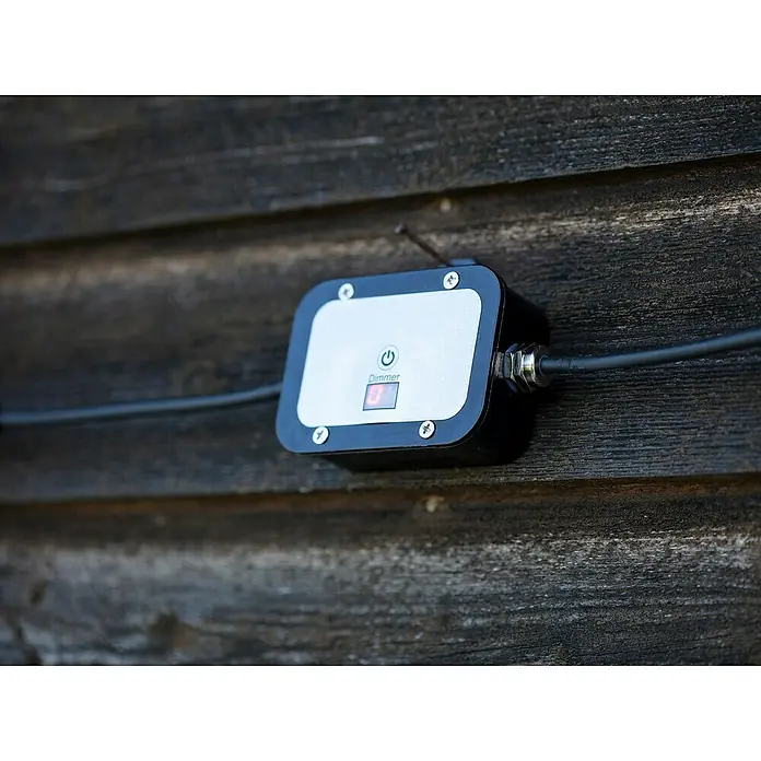 Garden 24 Bewegungsmelder Dimmer - Schwarz, L x B x H: 10 x 10 x 3,5 cm - Außenmontierter Dimmschalter mit schwarzem Gehäuse, silberner Frontplatte und LED-Anzeige, installiert an einer Holzwand.