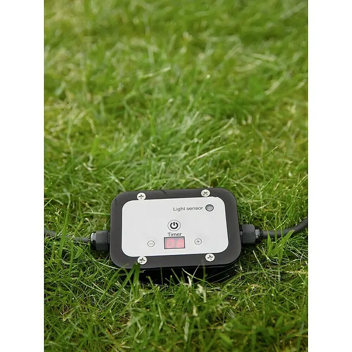 Garden 24 Bewegungsmelder Sensor/Timer - Schwarz, L x B x H: 10 x 10 x 3,5 cm - Das Bild zeigt einen Lichtsensor-Timer auf einer grünen Rasenfläche. Der Timer verfügt über Tasten zur Steuerung und ein Display zur Anzeige der Einstellungen.
