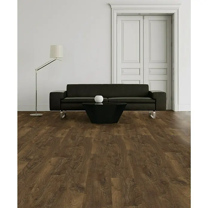 LOGOCLIC Laminado Roble Florencia - 1.380 x 193 x 10 mm, Roble, AC5 - Elegante salón con suelo laminado oscuro, sofá negro y lámpara de pie. El pavimento aporta calidez y estilo a la estancia.