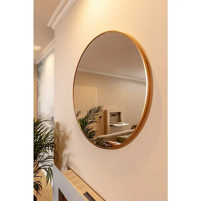 Rahmenspiegel Levi - Durchmesser: 80 cm, Gold, Metall - Runder Wandspiegel mit goldenem Rahmen. Der Spiegel reflektiert einen Teil des Wohnzimmers mit Pflanze, Sofa und Schrank.