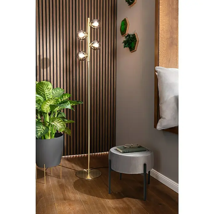 Lucide Tycho StehleuchteHöhe: 154 cm, Gold - Eine moderne Stehlampe mit vier kugelförmigen Lampenschirmen neben einem Hocker und einer Pflanze.