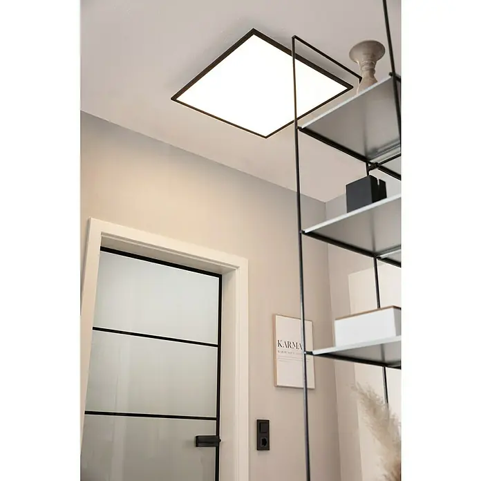 Tween Light LED-Panel CCT-RC-DIM32,5 W, L x B x H: 60 x 60 x 5 cm - Ein quadratischer Deckenleuchter mit schwarzem Rahmen erhellt den Raum, kombiniert mit einem schwarzen Regal an der Wand für modernes Design.
