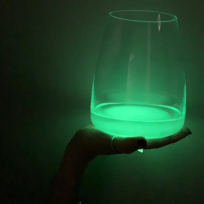 Fleur Pigmento concentrado Polvo fotoluminiscente - Fluor, 5 g - Esta imagen muestra un vaso iluminado con un líquido verde, sostenido por una mano, creando un brillo cautivador.