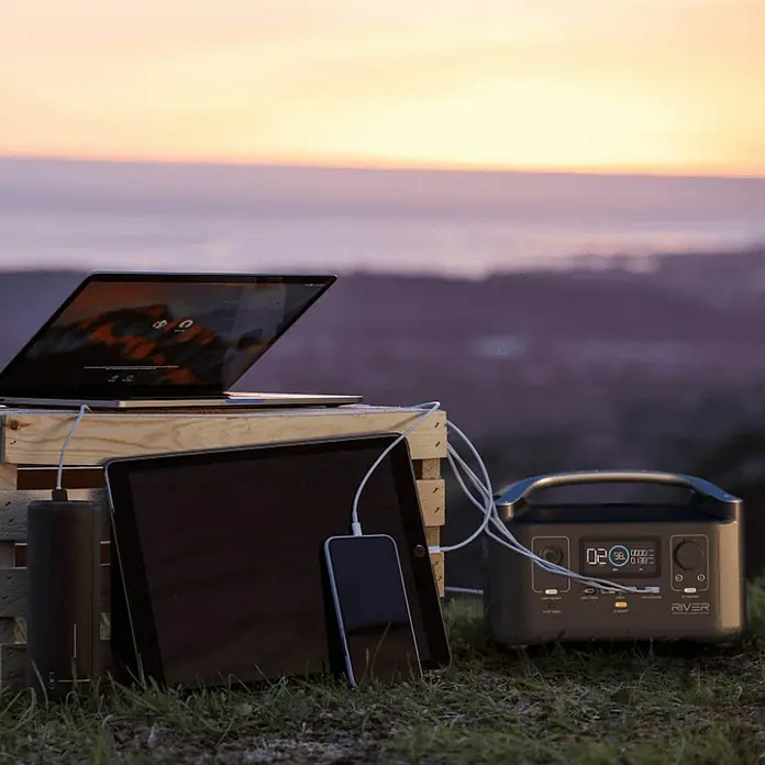 EcoFlow Estación de energía portátil River 600 - 288 Wh, Negro - La estación de energía EcoFlow River carga un ordenador portátil, una tableta y un teléfono con energía sostenible mientras el sol se pone en el horizonte.