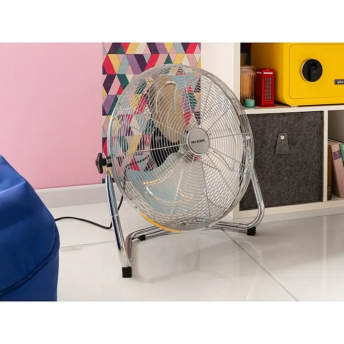 Proklima Bodenventilator - Silber, 45 cm - Ein chromfarbener Pro Klima Ventilator steht vor einer farbenfrohen Wand und einem weißen Regal. Der Ventilator hat ein modernes Design.