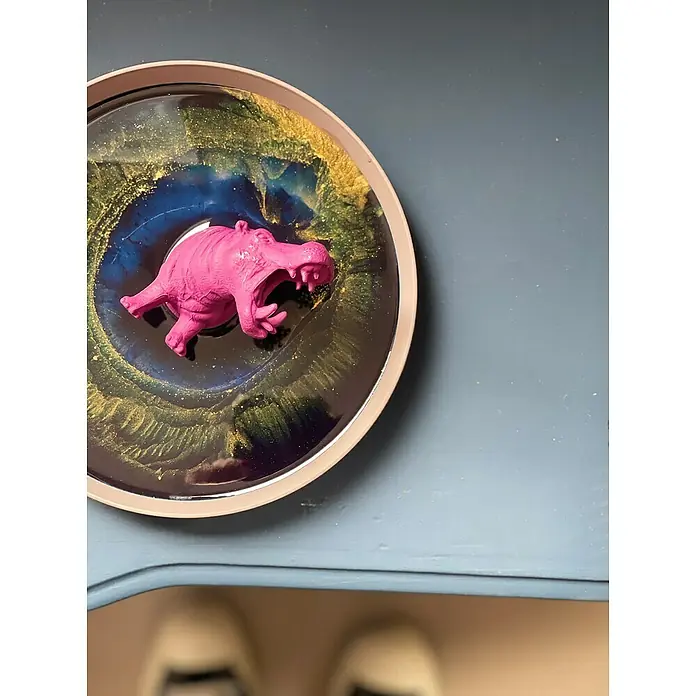 Fleur Colorante líquido para resina - Marrón chocolate, 10 ml - Un plato decorativo de resina con un hipopótamo rosa nadando en una mezcla arremolinada de azul, oro y negro.