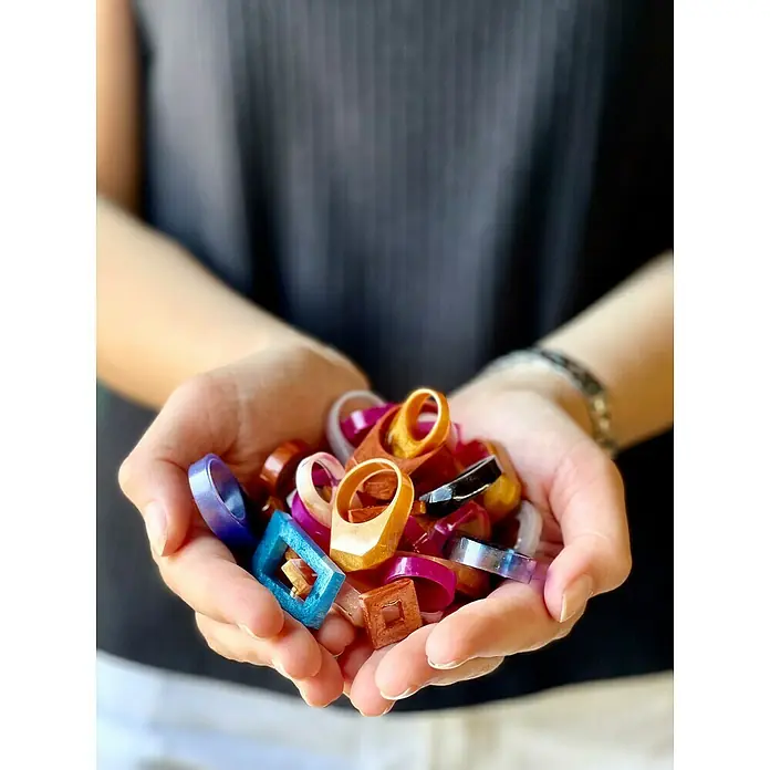 Fleur Molde Anillos - Silicona - Primer plano de unas manos que sostienen una variedad de anillos de resina modernos y coloridos de diferentes formas y diseños.