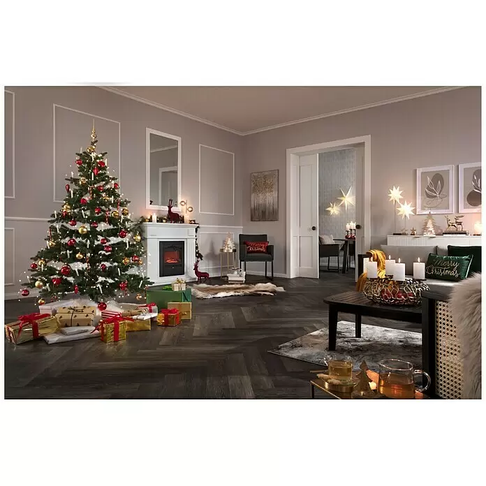 Stumpenkerzen-Set Rustic Safe Candle - 4 Stk., Ø x H: 6 x 11 cm, Wollweiß - Ein festliches Wohnzimmer, weihnachtlich dekoriert mit einem großen Baum, einem Kamin und verschiedenen Feiertagsdekorationen, einschließlich brennender Kerzen und Geschenken.