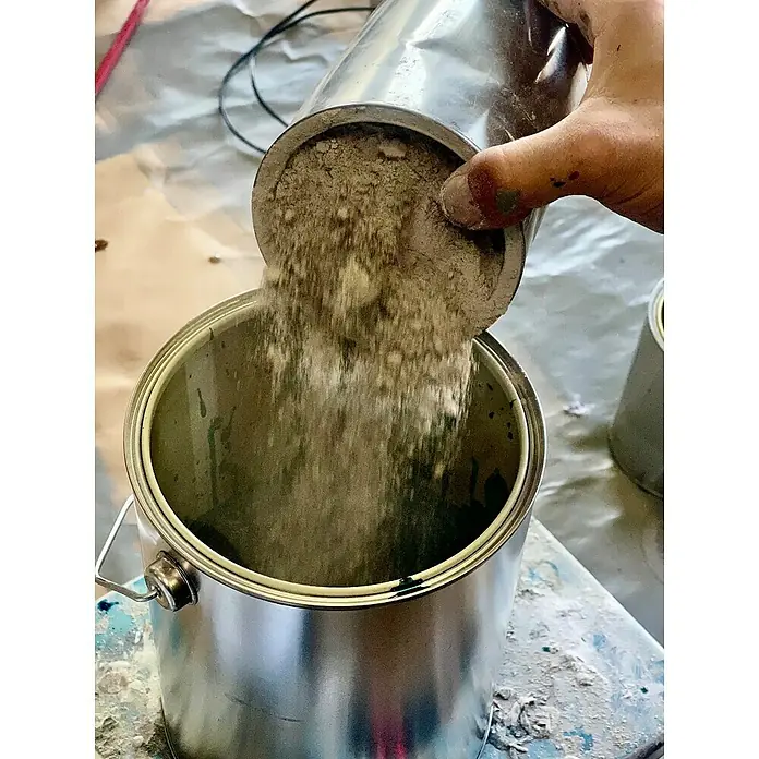 Fleur Kit Microcemento - Greige, 2 kg - Polvo vertido de una lata a otra, posiblemente para mezclar pinturas o hacer un revestimiento.