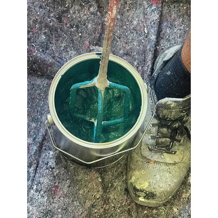 Fleur Kit Microcemento - Greige, 2 kg - Un bote de pintura lleno de pintura verde azulado y una herramienta para mezclar, colocado sobre una superficie salpicada, junto a un zapato sucio.