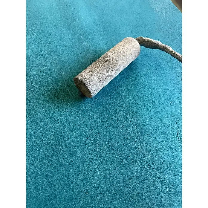 Fleur Kit Microcemento - Grey White, 8 kg - Primer plano de una herramienta de enlucido con cabeza cilíndrica y mango curvo, sobre una superficie verde azulada.