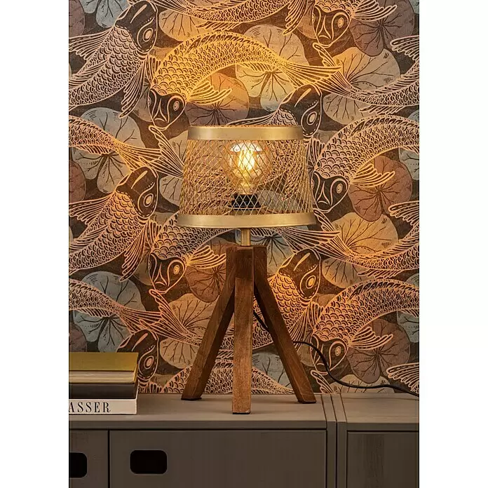 A.S. Création Metropolitan Stories II Vliestapete Koi - Blau, Tieroptik, 10,05 x 0,53 m - Eine Tischlampe mit Holz-Dreibeinfuß und goldenem Netzschirm steht auf einem dunkelgrauen Schrank neben Büchern vor gemusterter Tapete.