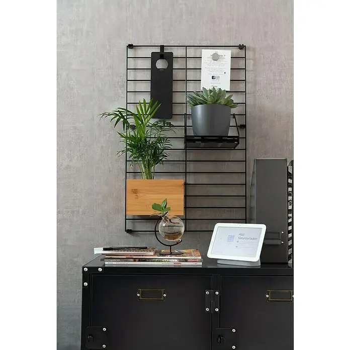 Rasch LOFT Vliestapete Uni - Grau, Betonoptik, 10,05 x 0,53 m - Eine schwarze Gitterwand mit Pflanzen, einem schwarzen Schild und einem Smart Display auf einem schwarzen Schrank.