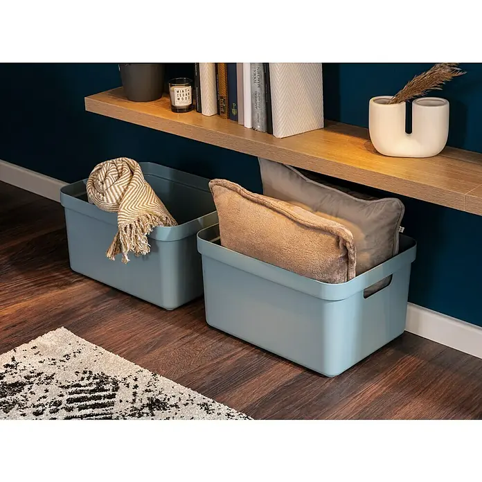 Sunware Aufbewahrungsbox Sigma Home - L x B x H: 35 x 24,6 x 18,3 cm, Kunststoff, Blaugrau - Zwei hellblaue Aufbewahrungsboxen mit Decken und Kissen darunter, auf einem Holzboden und einer weißen Bordüre.