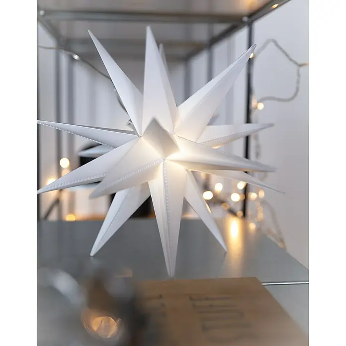 Tween Light LED-Stern 3D Kunststoff hängend - 50 cm, Weiß, Lichtfarbe: Warmweiß, IP44, Netzbetrieben - Nahaufnahme eines leuchtenden, weißen Papiersterns auf einem Regal, der eine festliche Atmosphäre schafft.