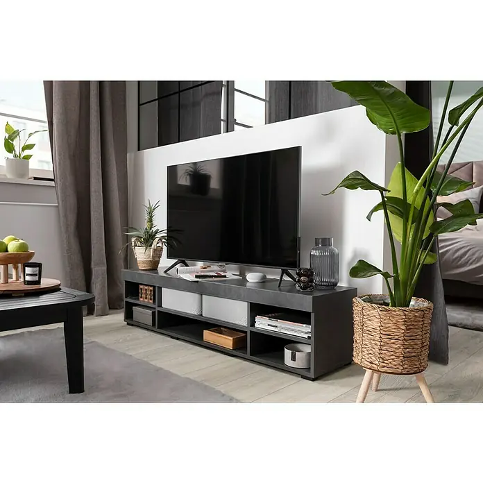 Elbersdrucke Verdunkelungsvorhang Sundown - Grau, B x H: 140 x 255 cm, 100 % Polyester - Wohnzimmer mit modernem TV-Schrank in Grau, auf dem ein großer Flachbildfernseher steht, umgeben von Pflanzen und Deko-Objekten.