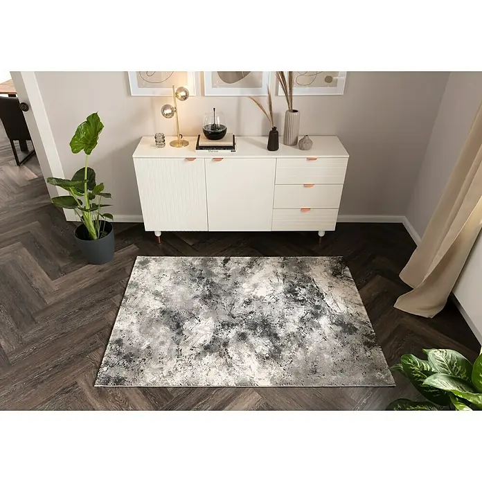 Kurzflorteppich Pablo 704 - Silber, 170 x 120 cm, 50% Polyester, 50% Polypropylen - Ein grauer Teppich mit abstraktem Muster liegt vor einem weißen Sideboard auf einem dunklen Holzboden und verleiht dem Raum einen modernen Touch.