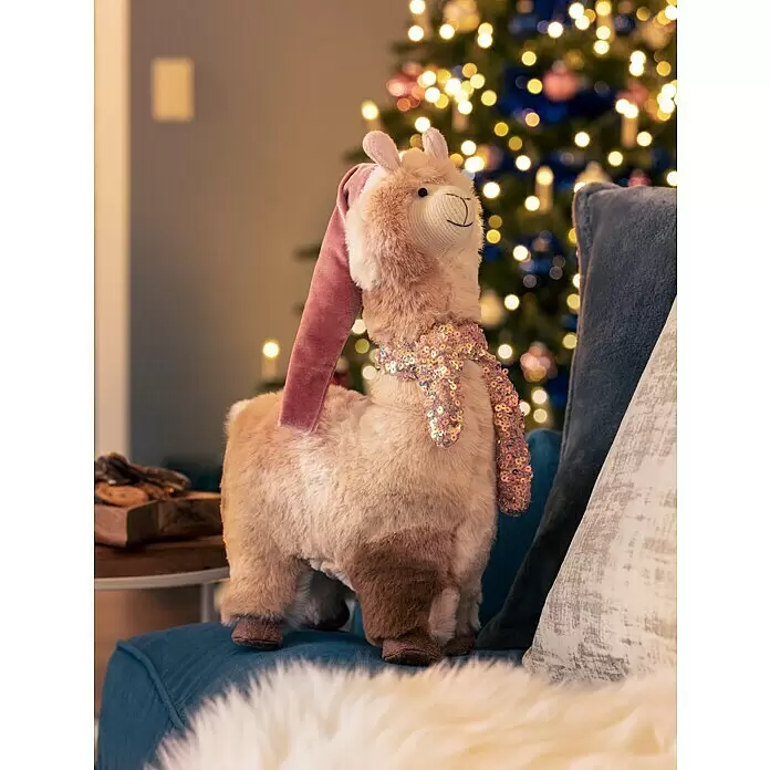 Dekofigur Weihnachtslama - L x B x H: 23 x 13 x 42 cm, Textil, Weihnachtswichtel, Schneemann - Ein festliches Plüsch-Lama in Hellbraun mit dunklen Akzenten, das einen rosa Samthut und einen funkelnden Paillettenschal auf einem blauen, flauschigen Stuhl trägt.