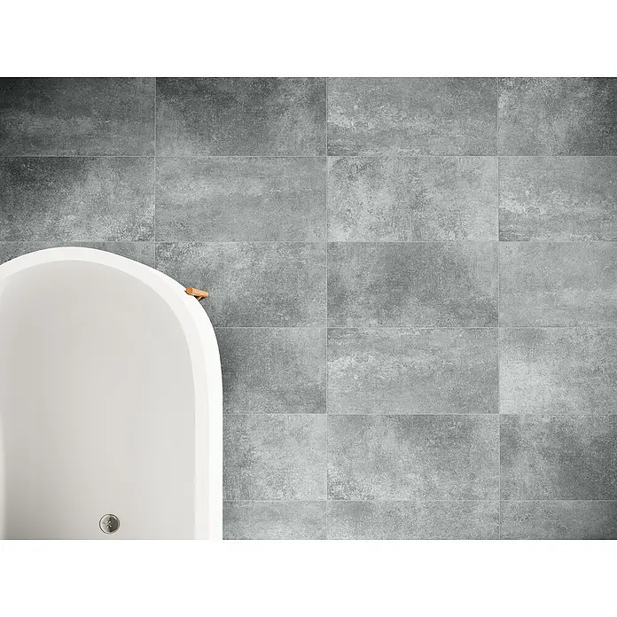 Domicil Feinsteinzeugfliese Living Concrete - 30 x 60 cm, Grau, Matt - Nahaufnahme einer modernen Badewanne vor einer grauen gefliesten Wand, die ein elegantes und minimalistisches Design zeigt.