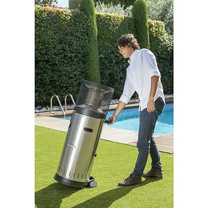 Enders Estufa de exterior Polo - 3 kW - 6 kW, Altura: 115 cm - Un hombre mueve un calentador de patio plateado sobre ruedas al aire libre. Está equipado con una malla de seguridad.
