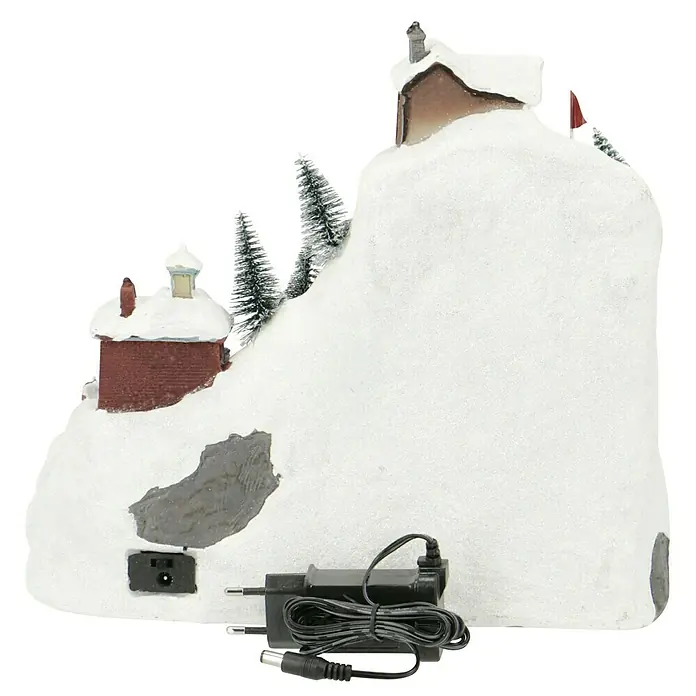 Konstsmide LED-Szenerie Skipiste - L x B x H: 31 x 20,5 x 27,5 cm, Bunt, Batteriebetrieben, LED - Eine verschneite Miniatur Winterdorf-Szene mit einem Haus und einer Kirche auf einem Hügel und einem schwarzen Netzteil.