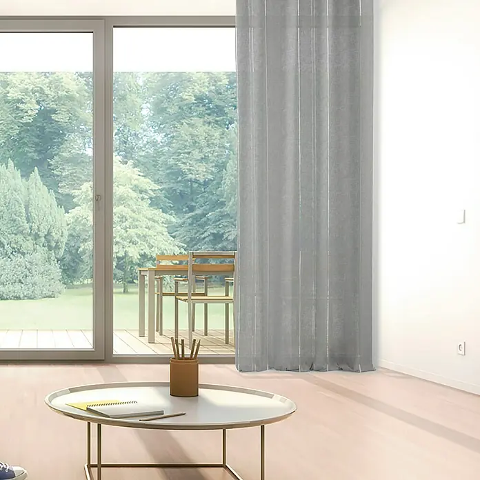Visillo para ventana Ophelie - 140 x 250 cm, 100% poliéster, Gris - Una cortina gris frente a una ventana con vista a zonas verdes, una mesa de centro con bolígrafos y un bloc de notas en primer plano.