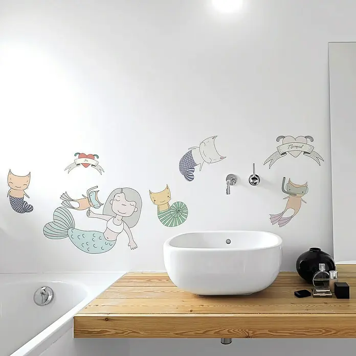 Vinilo de pared Sirenas - Multicolor, Plástico - Baño con paredes blancas, lavabo y encimera de madera, decorado con adhesivos de pared temáticos de sirenas que añaden un toque lúdico a la habitación.