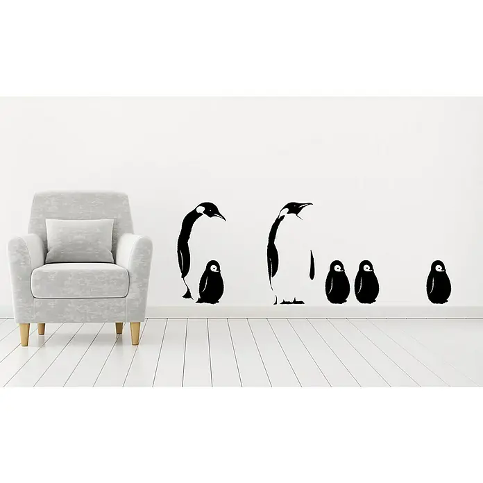 Vinilo de pared Pingüinos - 48 x 68 cm, Plástico - Un adhesivo de pared con pingüinos en negro se muestra en una pared blanca, junto a un sillón gris con un cojín.