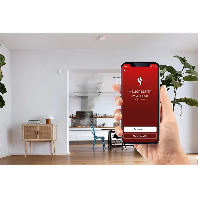 Bosch Smart Home Rauchwarnmelder II - Alarmsignal: 85 dB - Ein Smartphone zeigt eine Rauchwarnmeldung in einem hellen Wohnraum mit Rauchentwicklung im Hintergrund, die auf ein Sicherheitsproblem hinweist.
