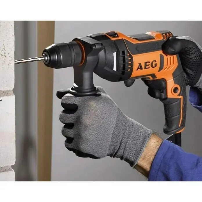 AEG Powertools Schlagbohrmaschine SBE 705 RE - 705 W, Schnellspannbohrfutter - Der AEG-Bohrhammer wird von einer Person mit Handschuhen bedient, um in eine Mauer zu bohren. Das Werkzeug ist orange und schwarz.