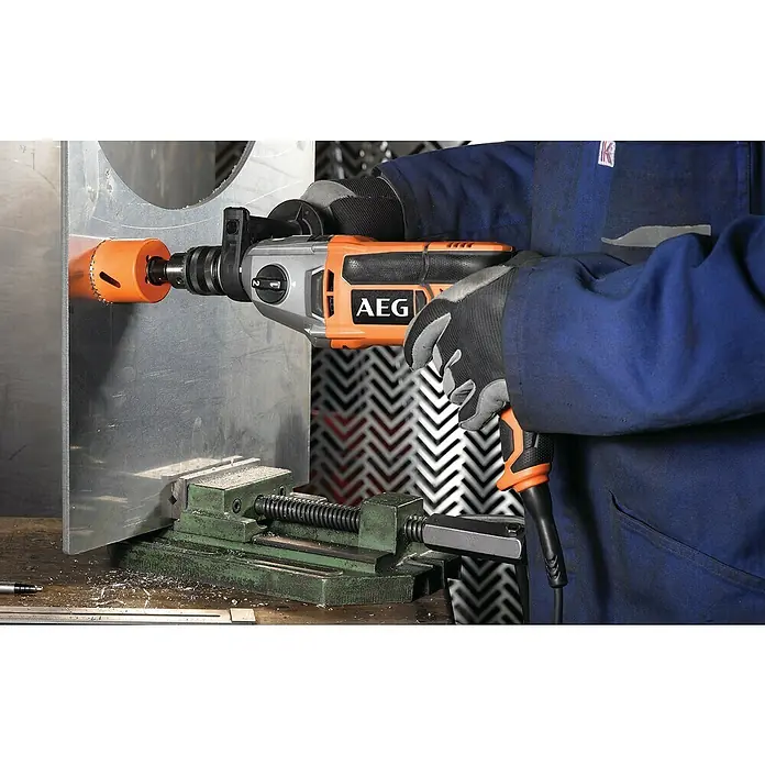 AEG Powertools Schlagbohrmaschine SB2E 1100 RV - 1.100 W, Schnellspannbohrfutter - Ein AEG-Bohrgerät bohrt ein Loch in eine Metallplatte, die mit einem Schraubstock befestigt ist. Der Bohrer ist orange und schwarz.