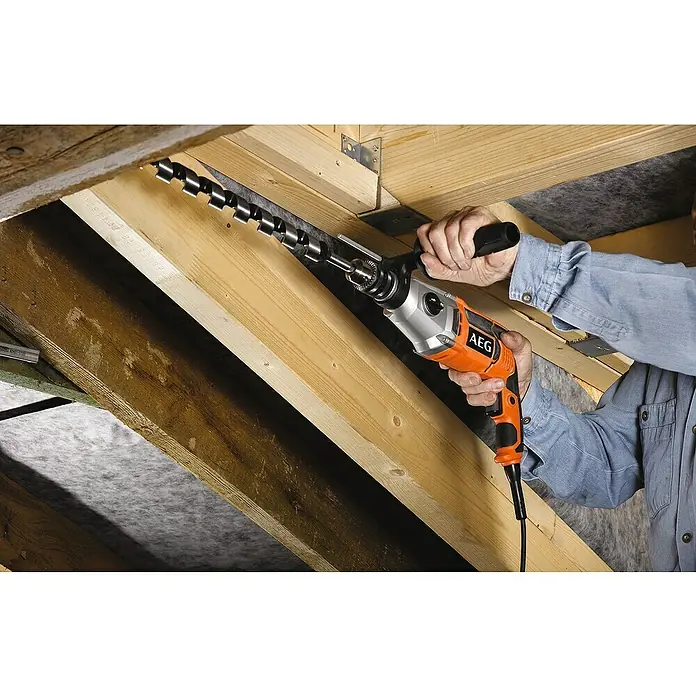 AEG Powertools Schlagbohrmaschine SB2E 1100 RV - 1.100 W, Schnellspannbohrfutter - Ein Handwerker bohrt mit einer AEG Bohrmaschine und einem langen Bohrer ein Loch in einen Holzbalken. Die AEG Bohrmaschine ist orange und silber.