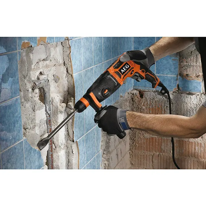 AEG Powertools Kombihammer KH 24 IXE - 800 W, 2,4 J, SDS-Plus-Aufnahme - Abgebildet ist ein AEG Bohrhammer in Aktion, der zum Entfernen von Fliesen verwendet wird. Ideal für Renovierungsarbeiten im Haus.