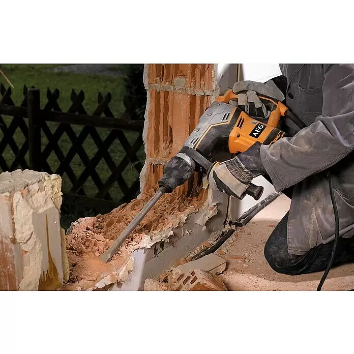 AEG Powertools Abbruchhammer MH 5 G - 1.100 W, 7,5 J, SDS-Max-Aufnahme - Eine Person benutzt einen orange-grauen AEG Bohrhammer, um eine Ziegelwand zu durchbrechen und Schutt zu erzeugen.