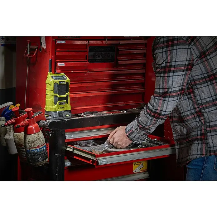 Ryobi ONE+ Radio Bluetooth de batería R18R-0 - Frecuencia: 87,5 - 108,0 kHz (FM) - Una radio Ryobi amarilla con Bluetooth está colocada sobre un carro de herramientas mientras una persona busca en un cajón.