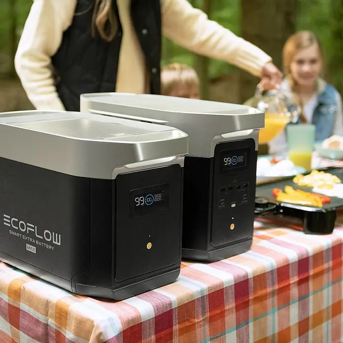 EcoFlow Estación de energía portátil Delta Max - 2.016 Wh, Negro - Dos baterías EcoFlow Smart Extra en una mesa al aire libre mientras la familia desayuna de fondo.