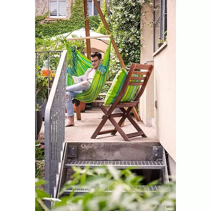 La Siesta Kissenhülle Amante - Lime, L x B: 50 x 50 cm - Mann entspannt in einem grün-gelb gestreiften Stoff-Hängesessel auf einer Terrasse.