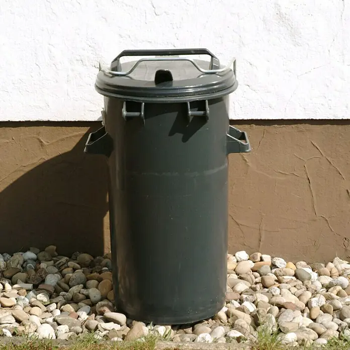 Floraworld Mülltonne Cargo - 50 l, Grau - Nahaufnahme eines grünen Abfallbehälters mit Deckel vor einer Wand auf einem Kiesuntergrund. Ideal für Gartenabfälle.