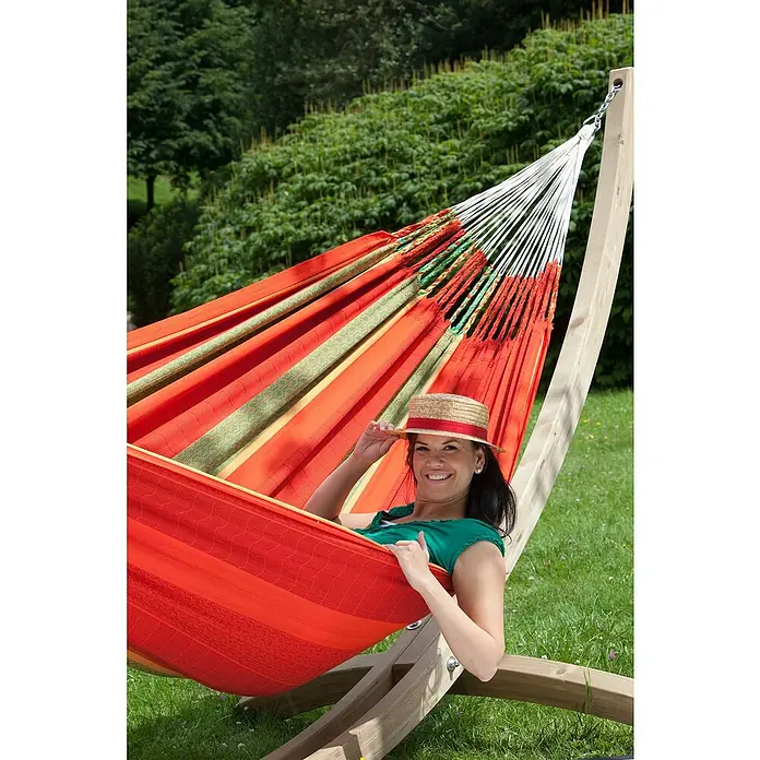 La Siesta Doppelhängematte Flora - L x B: 400 x 180 cm, Chili, Ausführungseigenschaft: Kingsize - Eine Frau entspannt in einer farbenfrohen Hängematte mit Holzgestell im Garten und genießt die Natur unter einem Strohhut.