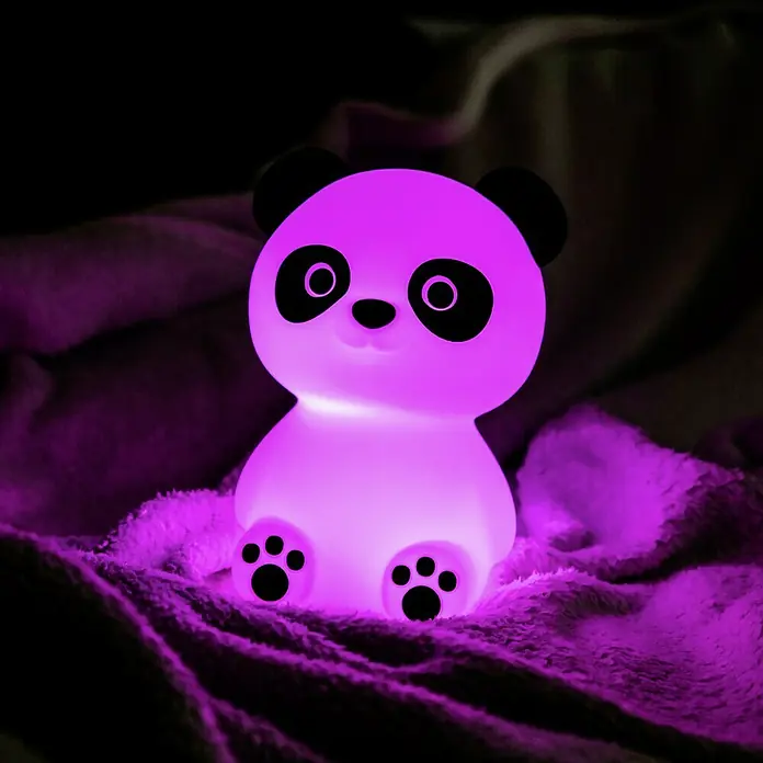 MegaLight LED-Nachtlicht PADDY PANDA - Weiß/Schwarz, L x B x H: 9 x 9 x 12 cm, RGBW, PADDY PANDA - Das Foto zeigt ein Panda-Nachtlicht, das in einem dunklen Raum auf einer weichen Decke sitzt und in einem hellen Lila leuchtet.