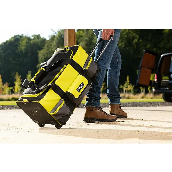Ryobi Werkzeugtasche RSSLTB2 - Polyester - Ein gelb-schwarzer RYOBI Rollenkoffer wird von einer Person in Jeans und Stiefeln auf einem Gehweg gezogen.