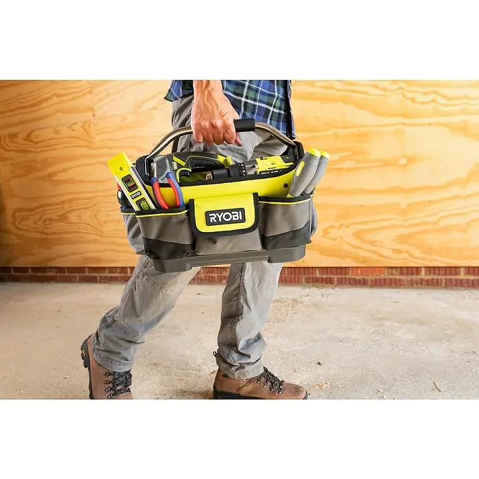Ryobi Werkzeugtasche RSSSOT1 S - Größe: S, Polyester - Nahaufnahme einer Person, die eine gelbe Ryobi Werkzeugtasche mit Werkzeugen vor einer hölzernen Wand und Ziegeln trägt.