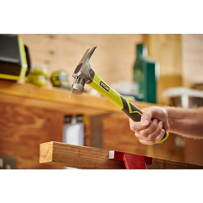 Ryobi Klauenhammer RH16FSS - Gewicht Kopf: 450 g, Stahl - Ein Ryobi Hammer mit einem Nagel, der in ein Stück Holz getrieben wird. Ideal für Bauprojekte und Heimwerkerarbeiten.