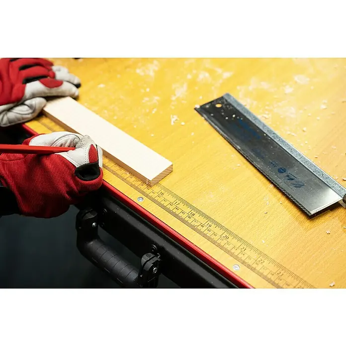 Werkbank Tragbar Duplex - L x B: 1.360 x 790 mm, Arbeitshöhe: 840 mm, Belastbarkeit: 150 kg - Nahaufnahme von Zimmermannshänden, die ein Holzstück mit einem Bleistift auf einem gelben Tisch neben einer Handsäge markieren.