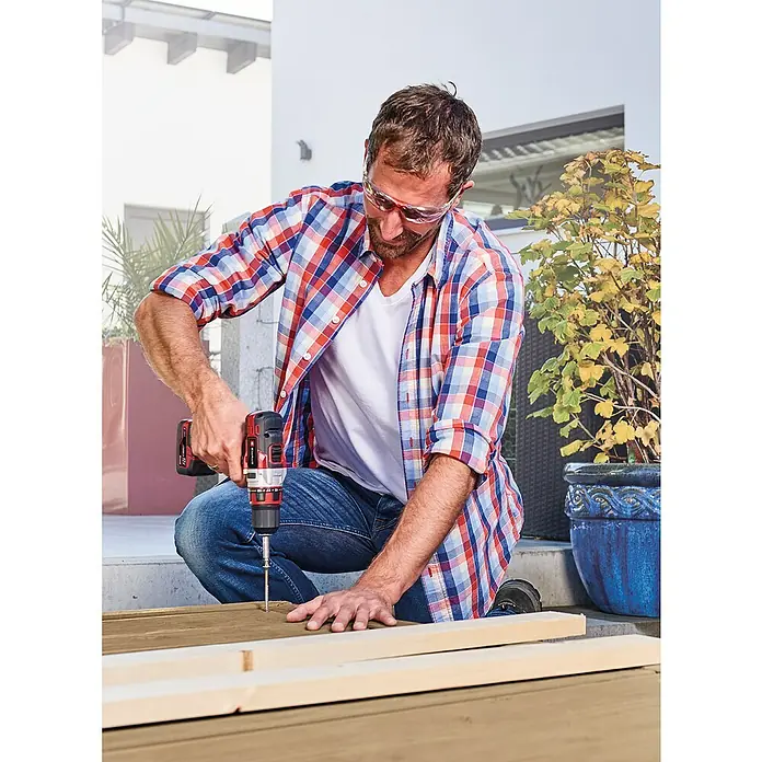 Einhell Set de taladro atornillador de batería TE-CD 12/1 Li + Lámpara 22+CL - 12 V, 2 baterías, 2 Ah - Un hombre con gafas y camisa a cuadros utiliza un taladro inalámbrico para trabajar la madera.