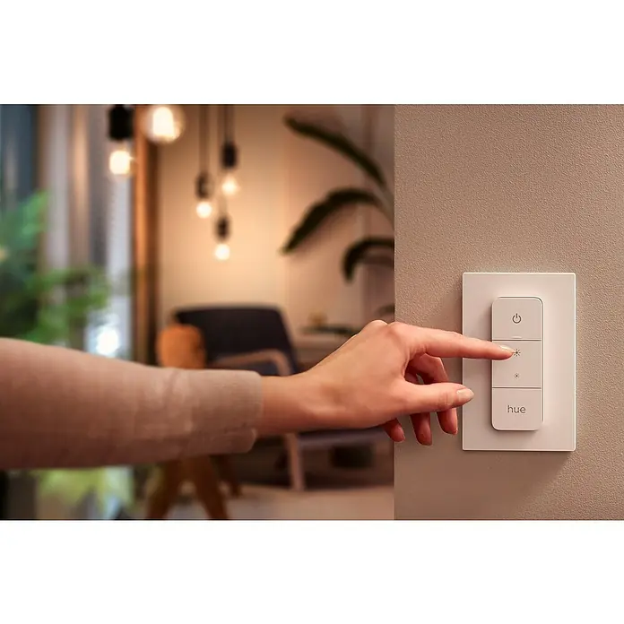 Philips Hue LED-Lampe WhiteE27, Dimmbar, Warmweiß, 1.055 lm, 9,5 W - Nahaufnahme einer Hand, die einen Philips Hue Dimmschalter an einer Wand betätigt, um die Beleuchtung im Raum anzupassen.