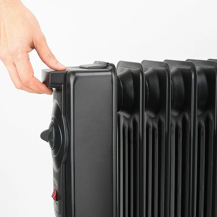 Black+Decker Ölradiator BXRA2300E - 2.300 W, Raumgröße bis ca. 23 m², Schwarz - Nahaufnahme einer Hand, die einen schwarzen Ölradiator berührt und seine Einstellungen anpasst. Heizgerät im Fokus.