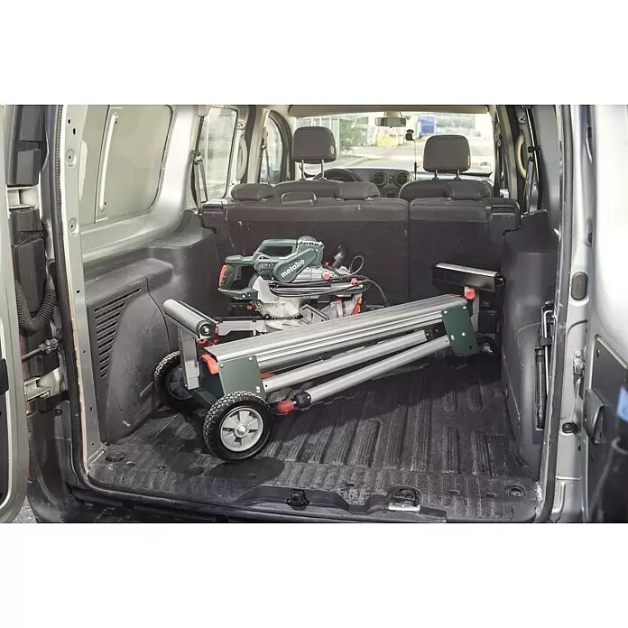 Metabo Sägetisch KSU 251 - Geeignet für: Kappsägen, Traglast: 250 kg - Eine grüne Metabo Kapp- und Gehrungssäge mit faltbarem silbernen Untergestell und roten Akzenten, kompakt im Kofferraum eines Transporters verstaut.